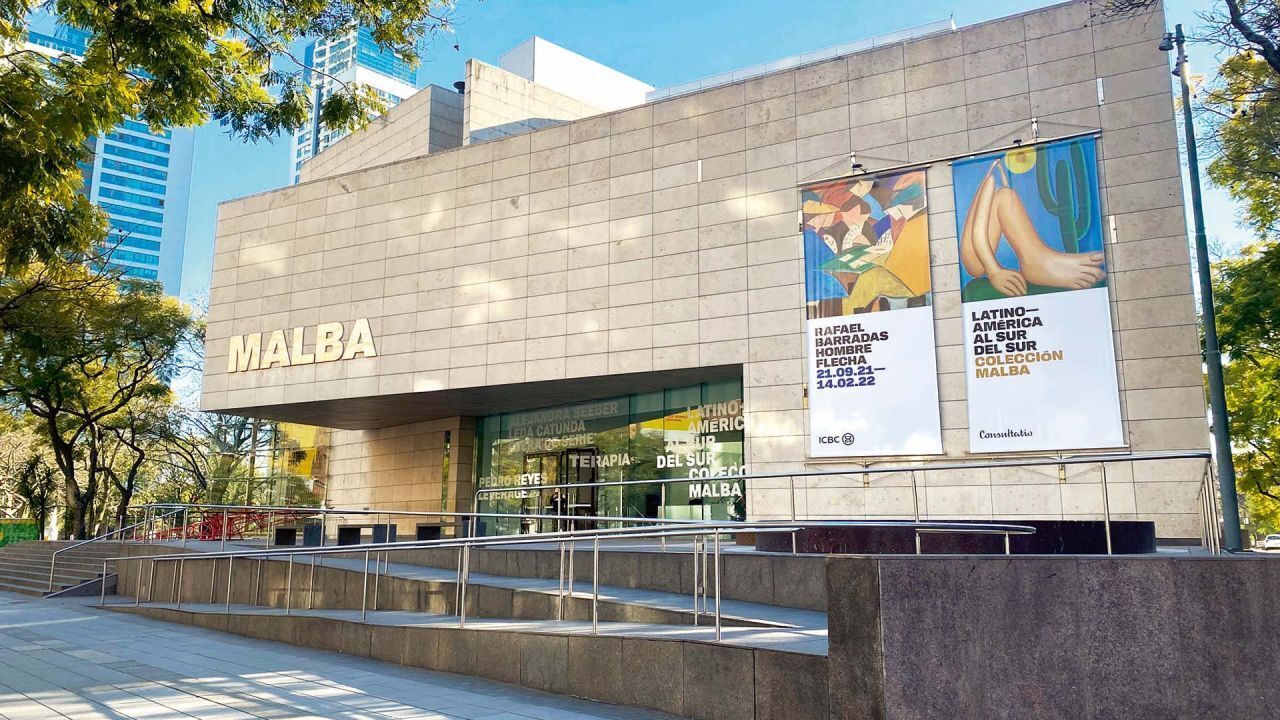 Um edifício com a placa 'MALBA' e dois grandes banners anunciando 'América Latina na Superfície' e 'Consulta'.