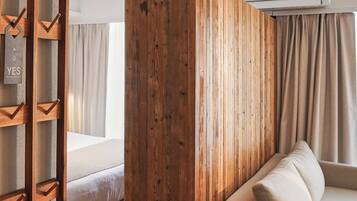 Una habitación de hotel con un panel de madera, una cama, un sofá y un ventanal con cortinas.