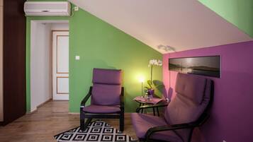 Une pièce avec deux fauteuils violets, une petite table sur laquelle est posée une orchidée en pot, un tableau encadré accroché au mur et un appareil de climatisation fixé au plafond.