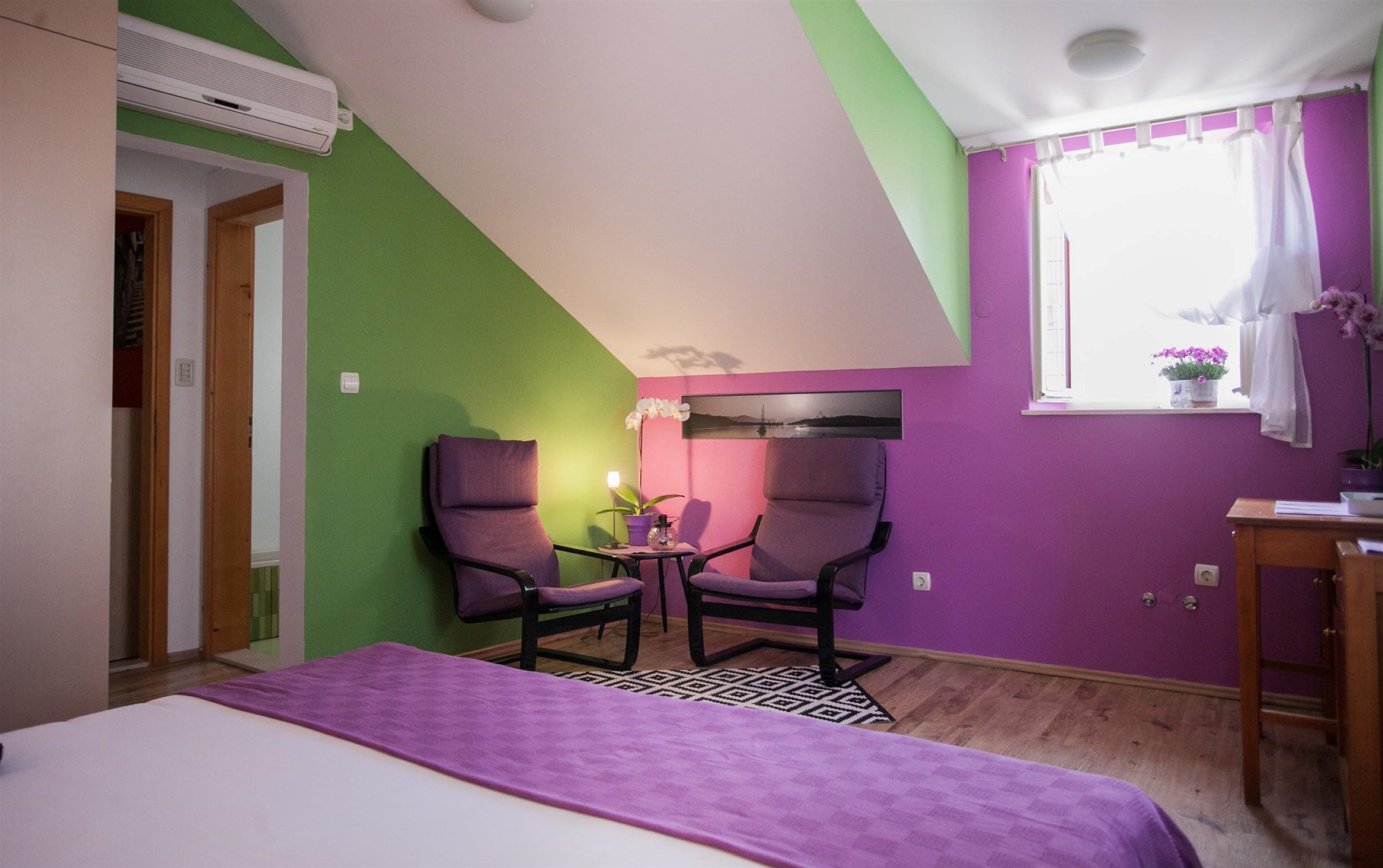 Une pièce comprenant un lit, deux chaises, une petite table, une fenêtre avec des rideaux et un climatiseur fixé au mur.