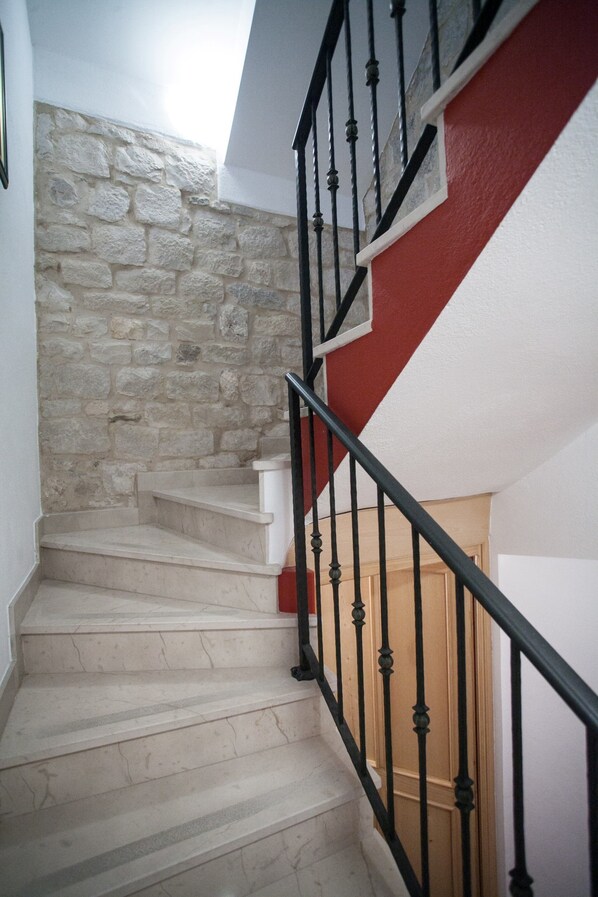 A staircase with stone walls and a red accent wall, leading to a wooden door. - Apartment and Room Ursa (Trogir)