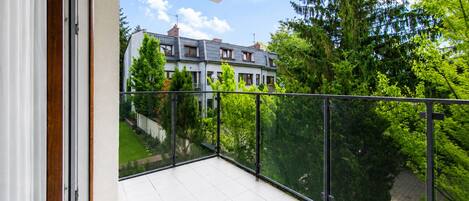 A balcony with a glass railing overlooking a residential area with trees and a house.