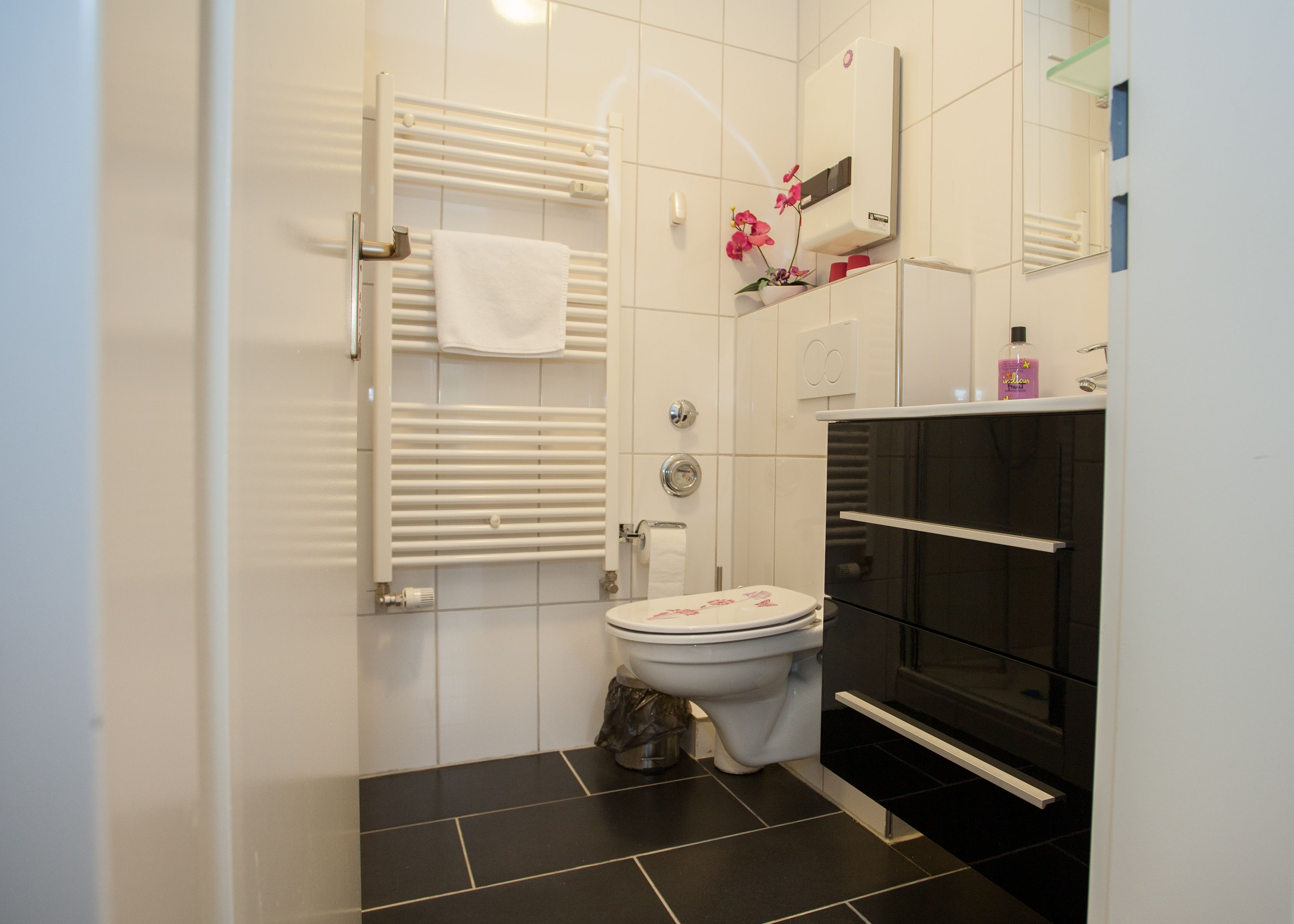 A modern bathroom with a toilet, a towel rack, a radiator, and a black bathtub.