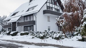 Une maison à deux étages, dotée d’un toit à forte pente, de plusieurs cheminées et d’un balcon.