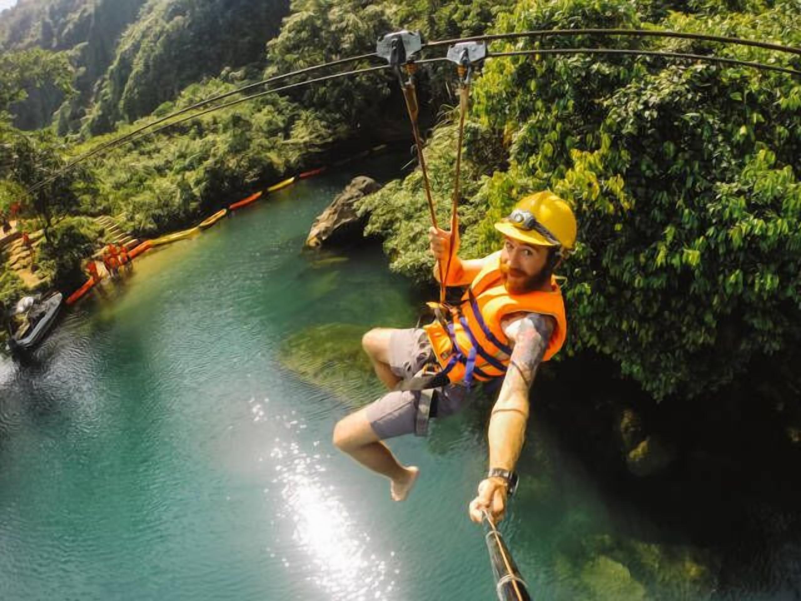 A person zip-lining over a river with lush greenery on either side.