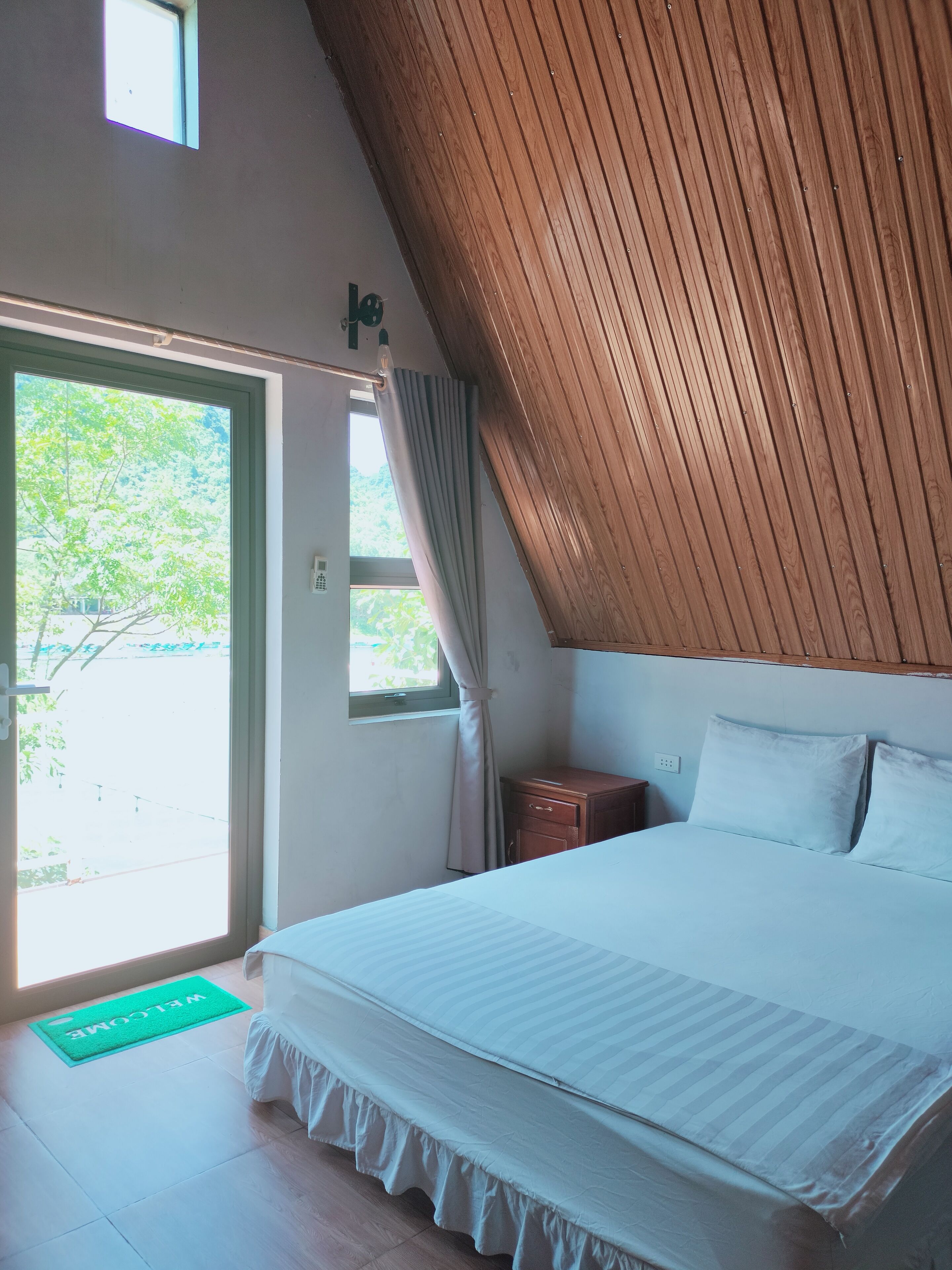 Una camera da letto con un letto grande, un soffitto spiovente in legno, una finestra con tende e un piccolo comodino.