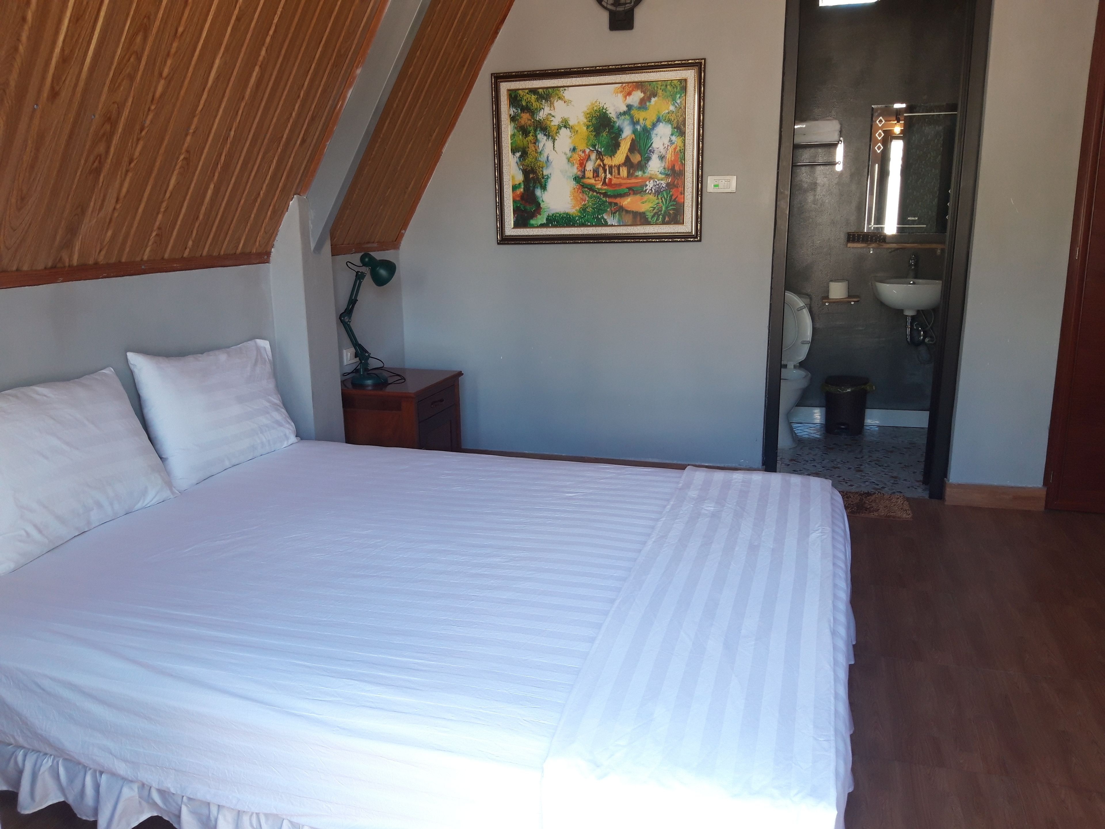 Quarto com uma cama grande, uma mesa de cabeceira, uma luminária de mesa e um quadro na parede.