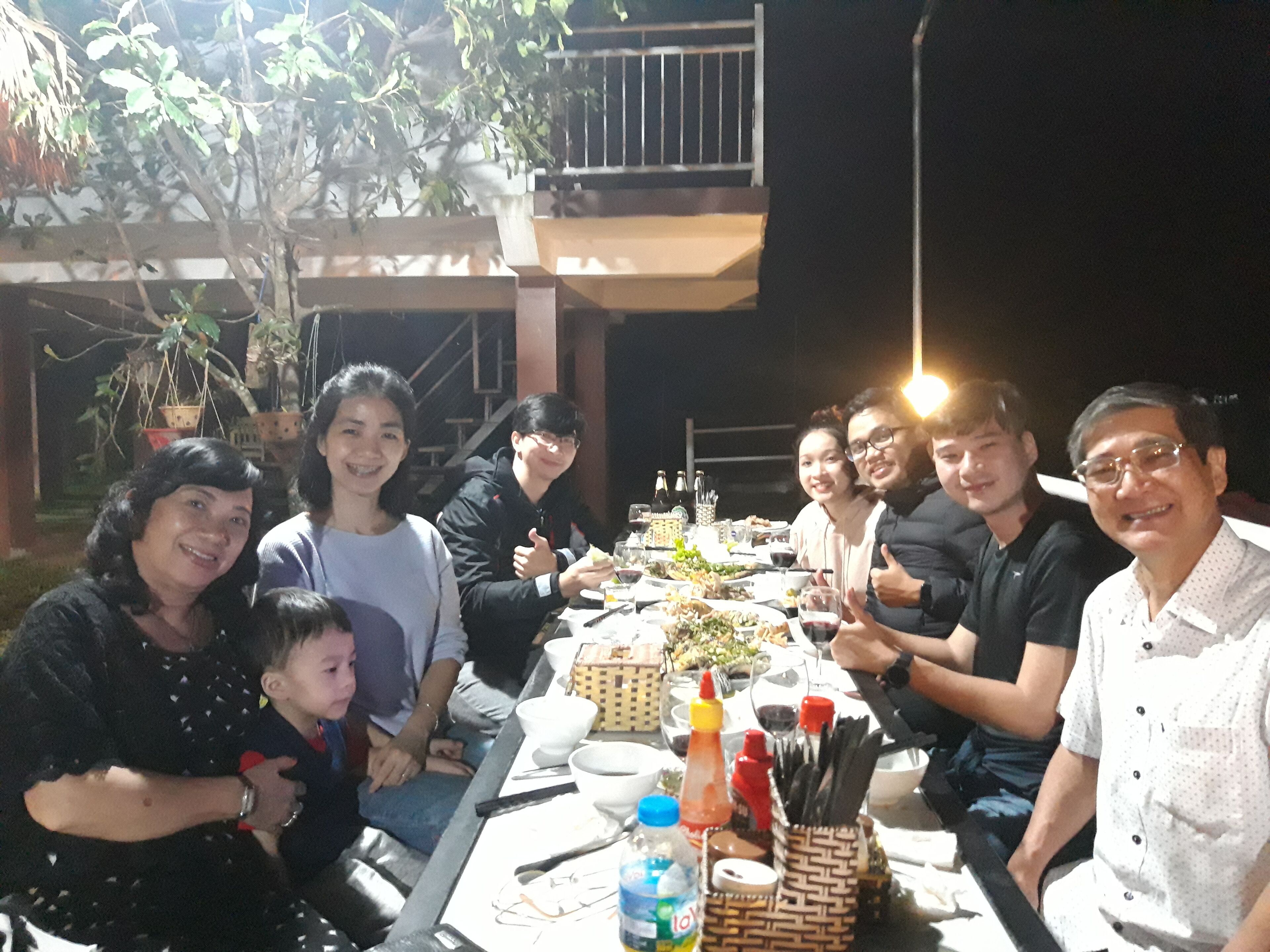 A group of people seated around a table with food and drinks, outdoors at night.