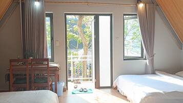 A room with two beds, a desk, and a chair. There is a sliding glass door leading to an outdoor area.