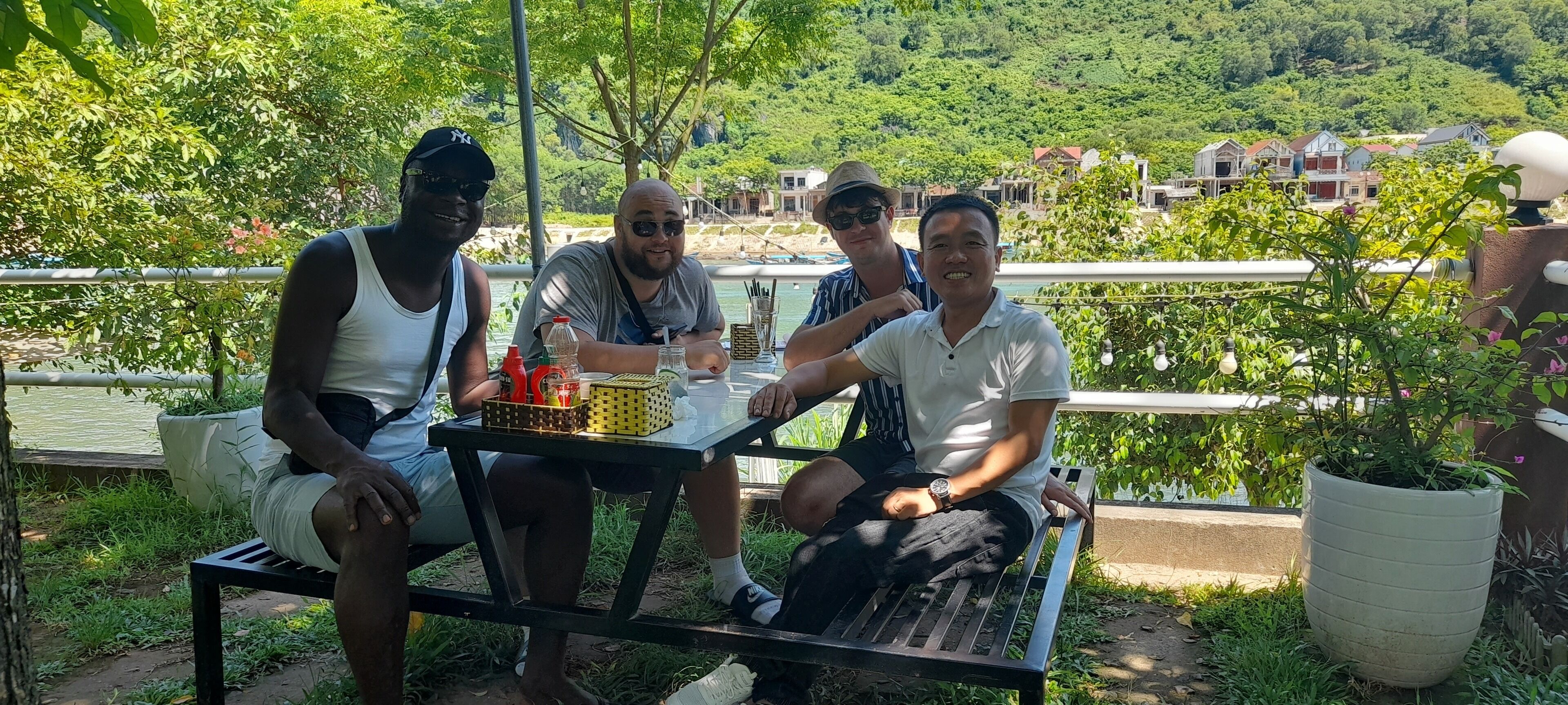 Three people seated at an outdoor table with a view of a lake and houses in the background.