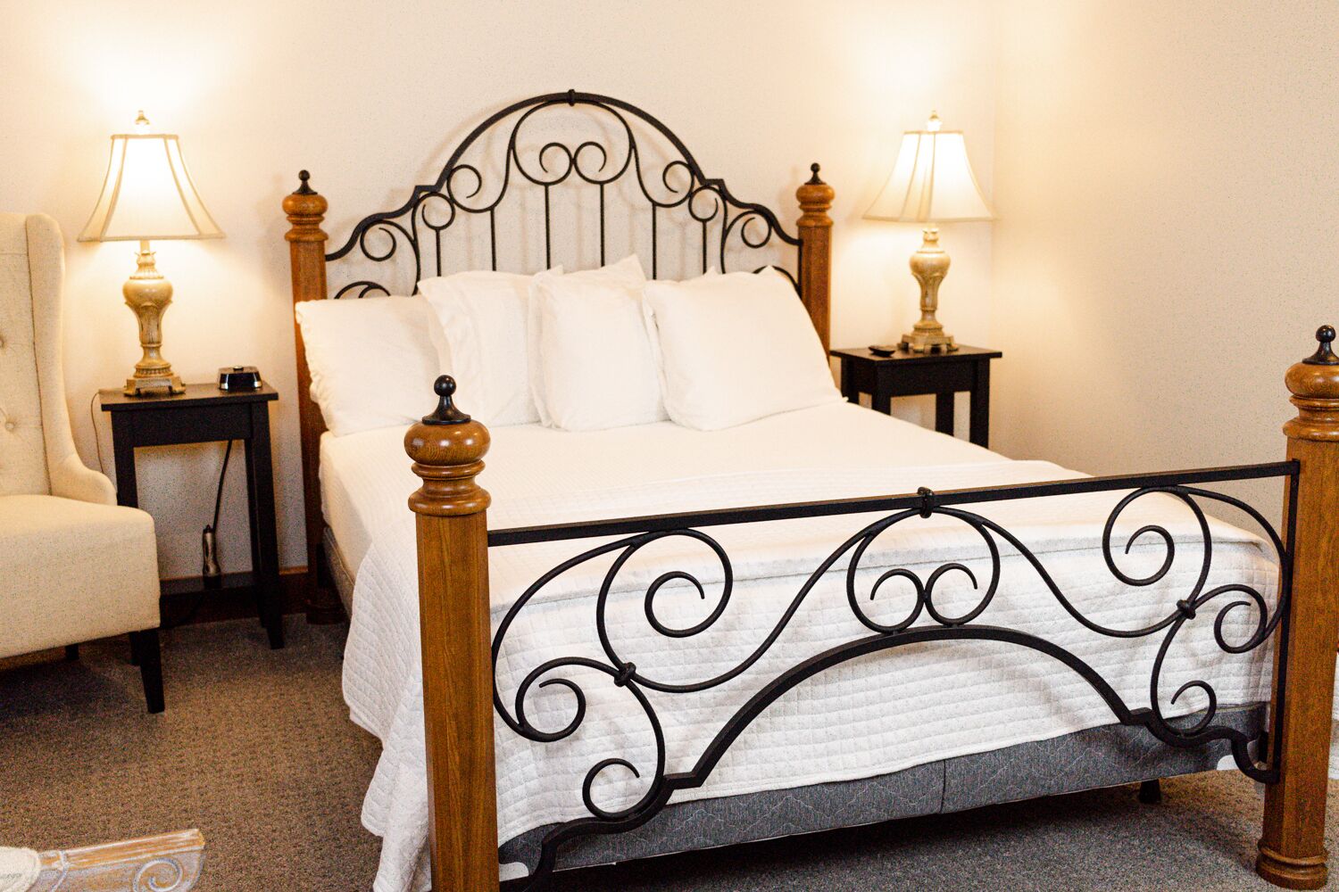 Una cama bien hecha con estructura de metal y cabecera de madera, flanqueada por dos mesitas de noche con lámparas.