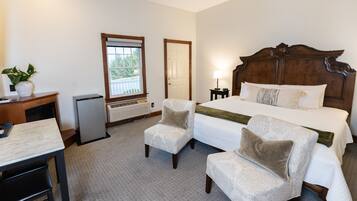 A hotel room with a large bed, two armchairs, a desk, and a small table. There is a window with a view of greenery outside.