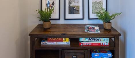 A hallway with framed artwork on the wall and a wooden console table with board games and potted plants.