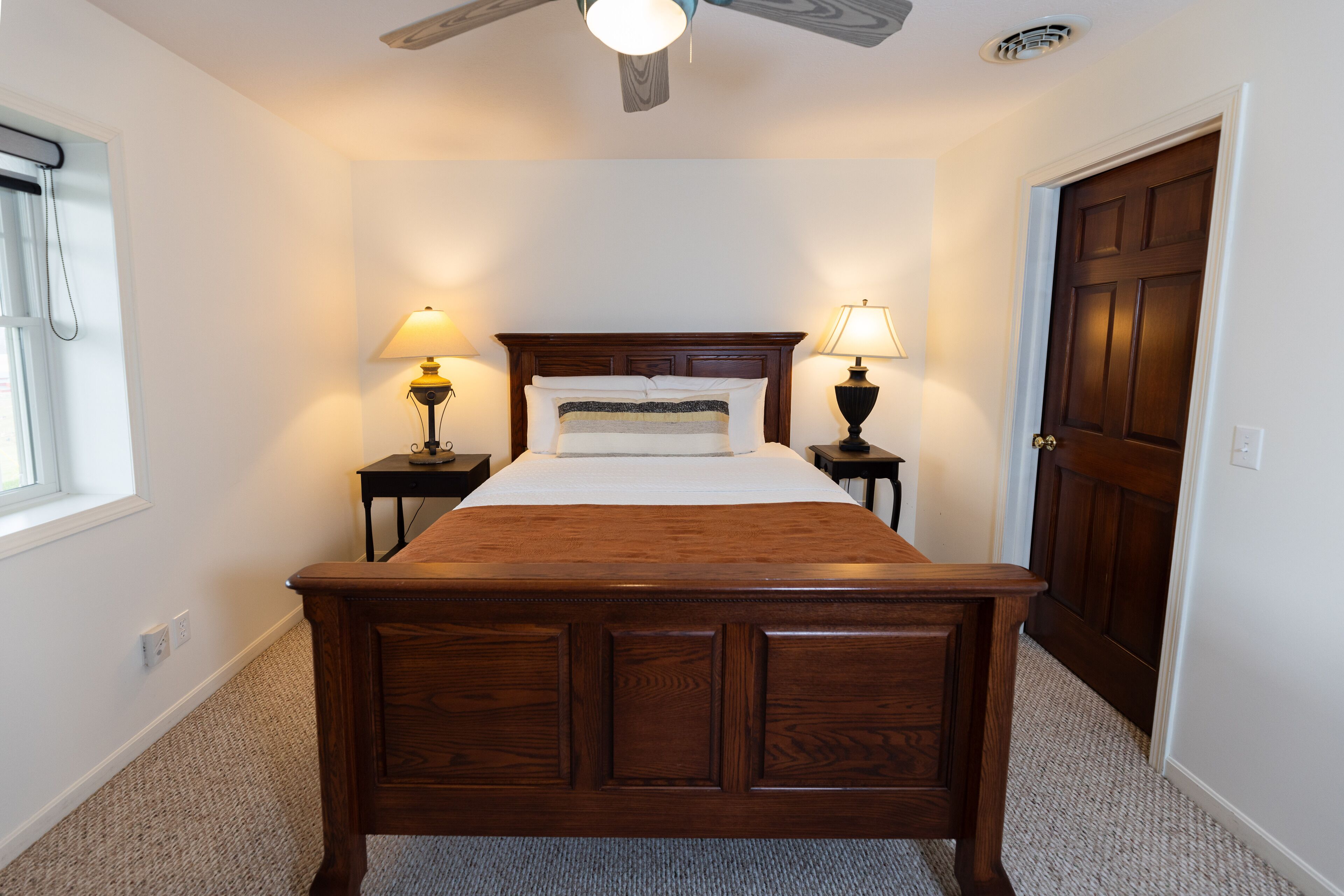 Un dormitorio con una cama de madera, dos lámparas de noche, un ventilador de techo y una puerta.