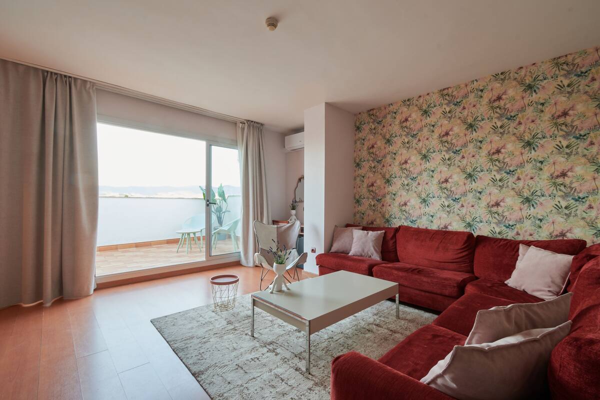 Un salón moderno con un sofá rojo, una mesa de centro blanca y vistas al mar a través de amplios ventanales.