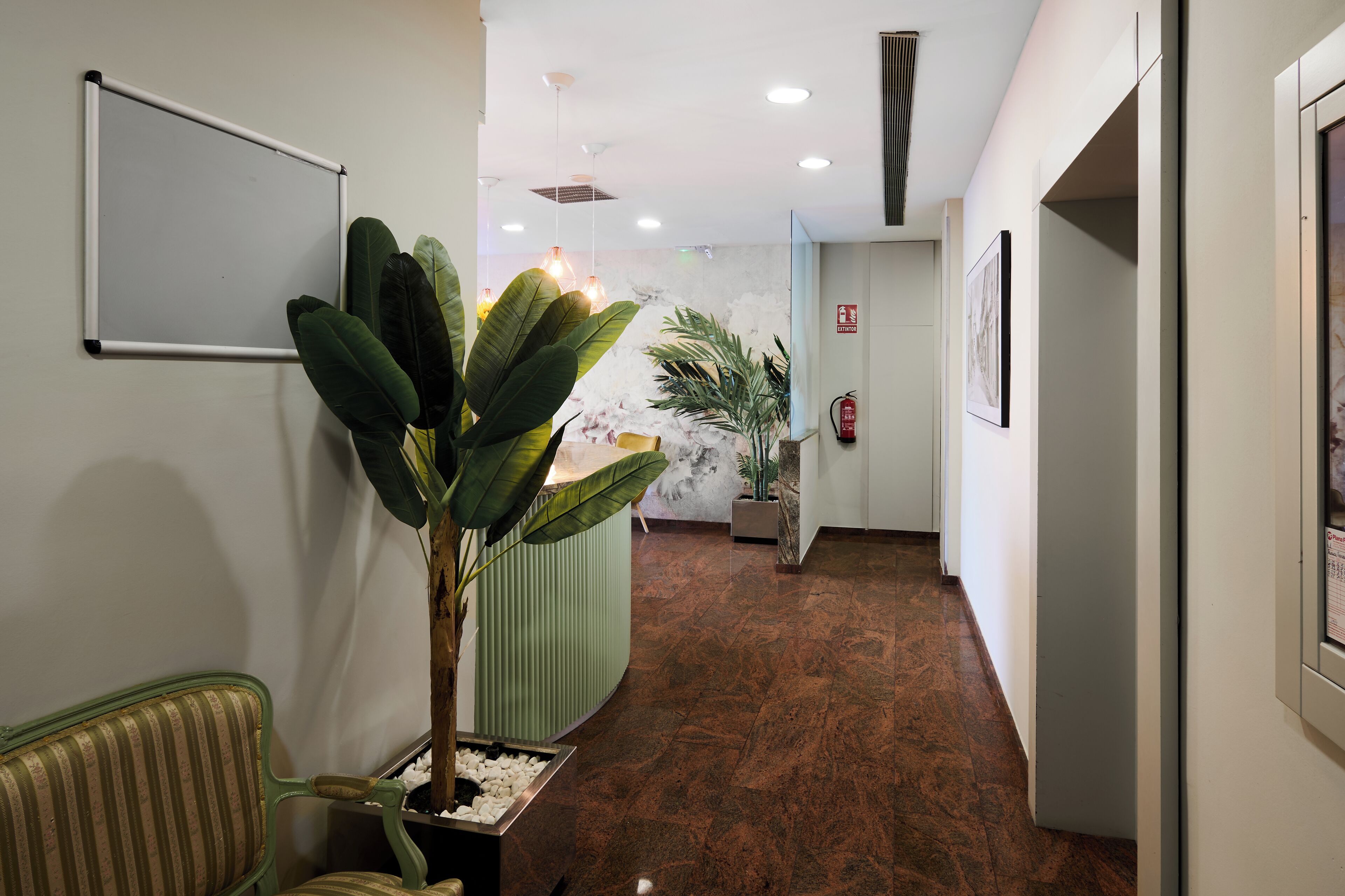 A reception area with a whiteboard, potted plants, a green bench, and a marble floor.