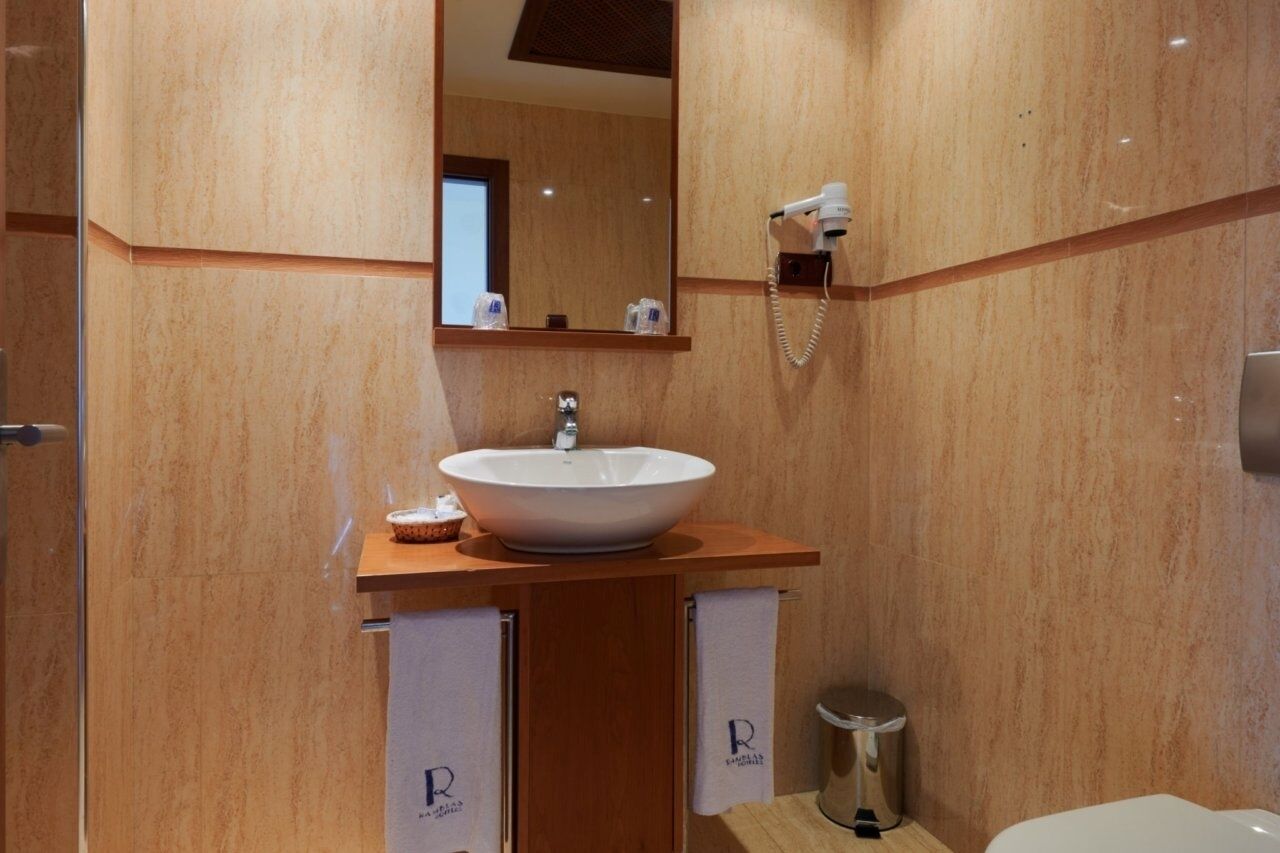 A modern bathroom with a large oval sink, a mirror, a hairdryer, and a trash bin.