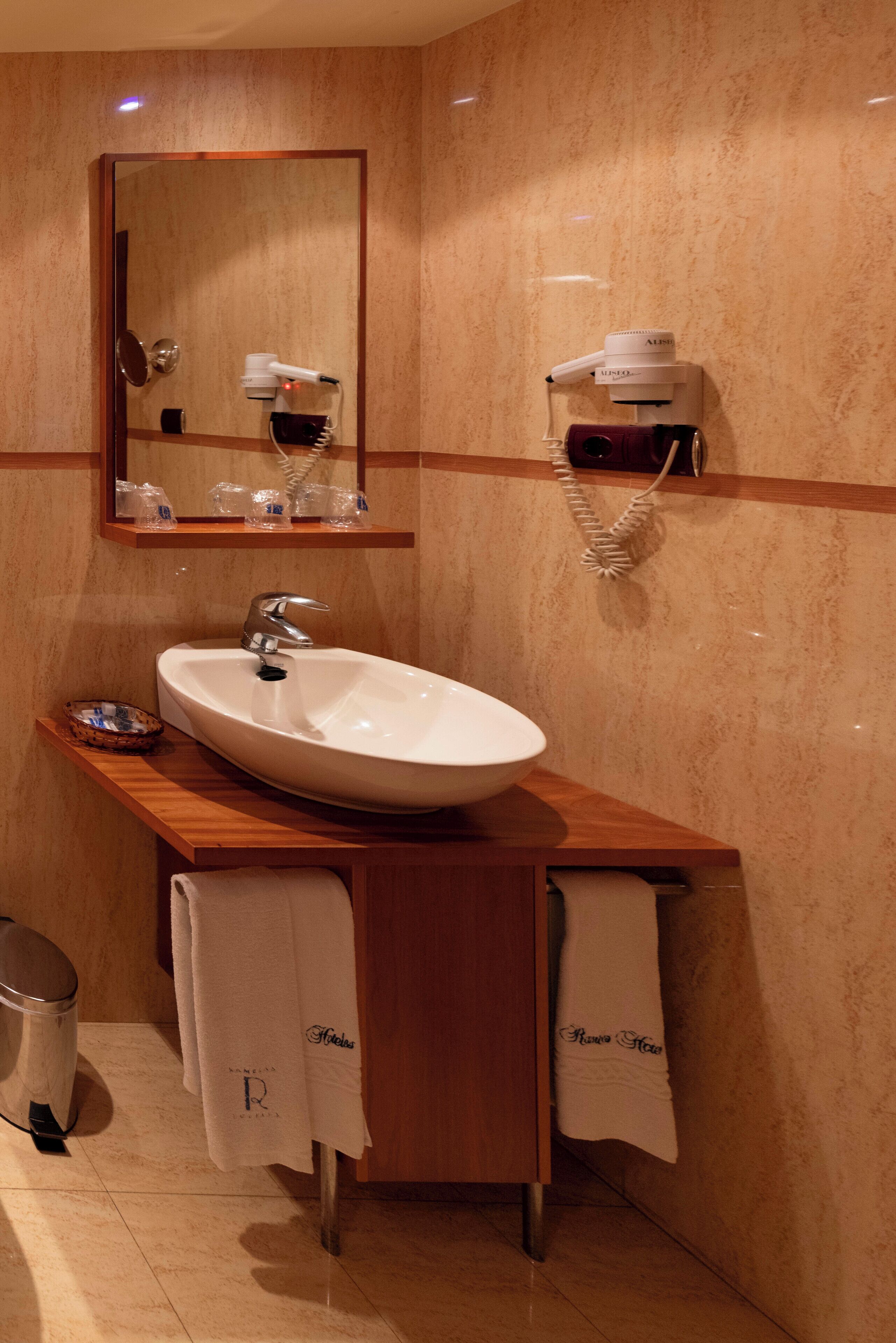 A bathroom with a large mirror, a white sink, a hairdryer, and a towel rack.