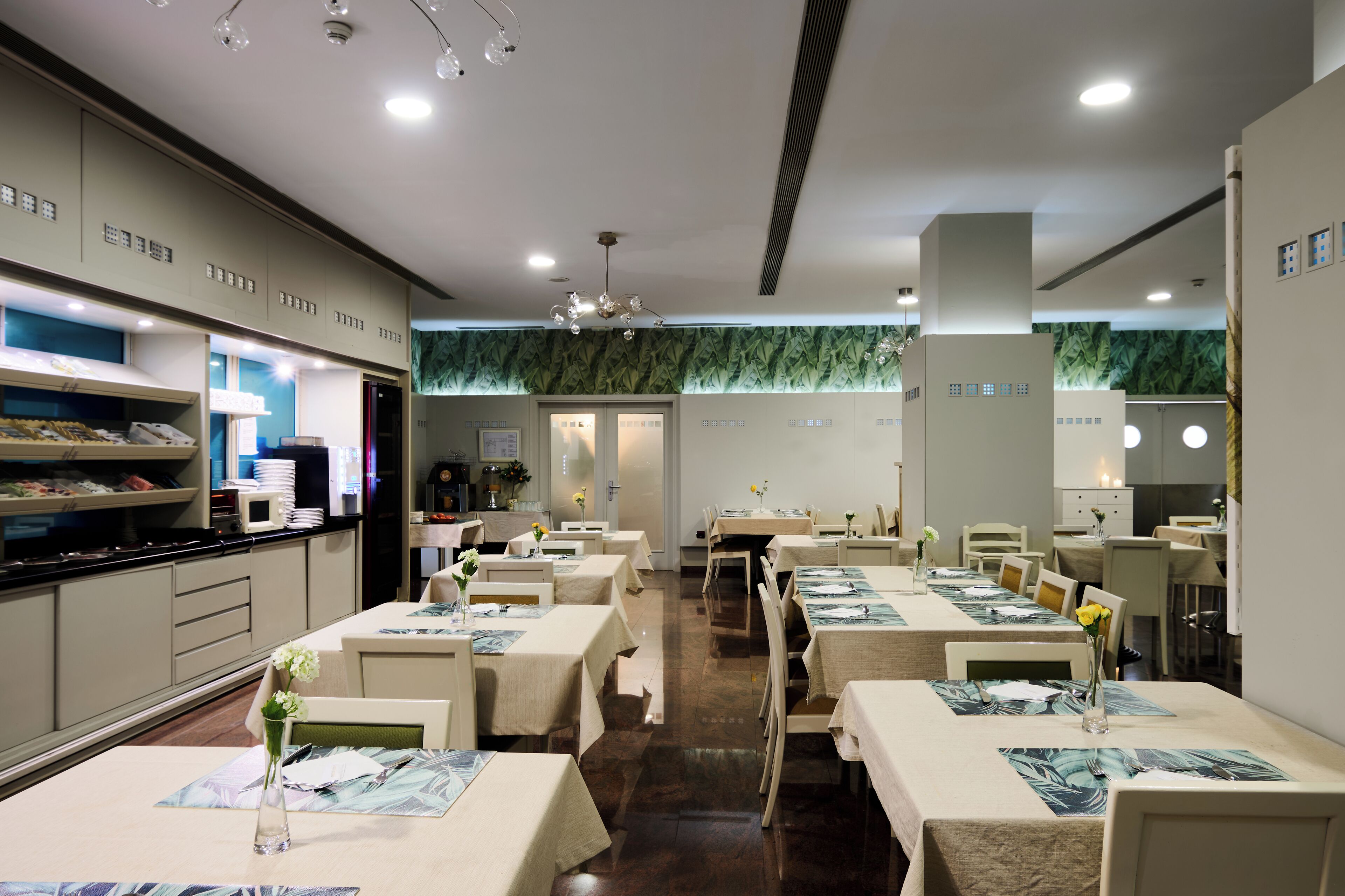 Un restaurant avec de nombreuses tables, chacune recouverte d’une nappe et agrémentée de couverts. Des chaises sont disposées autour des tables, et un comptoir présente une variété de plats.