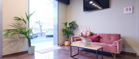 A modern lobby with a pink sofa, a coffee table, and potted plants.