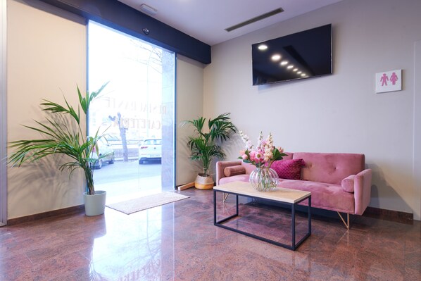 A modern lobby with a pink sofa, a coffee table, and potted plants.