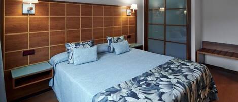 A hotel room with a large bed, wooden headboard, bedside lamps, a nightstand, and a sliding glass door.