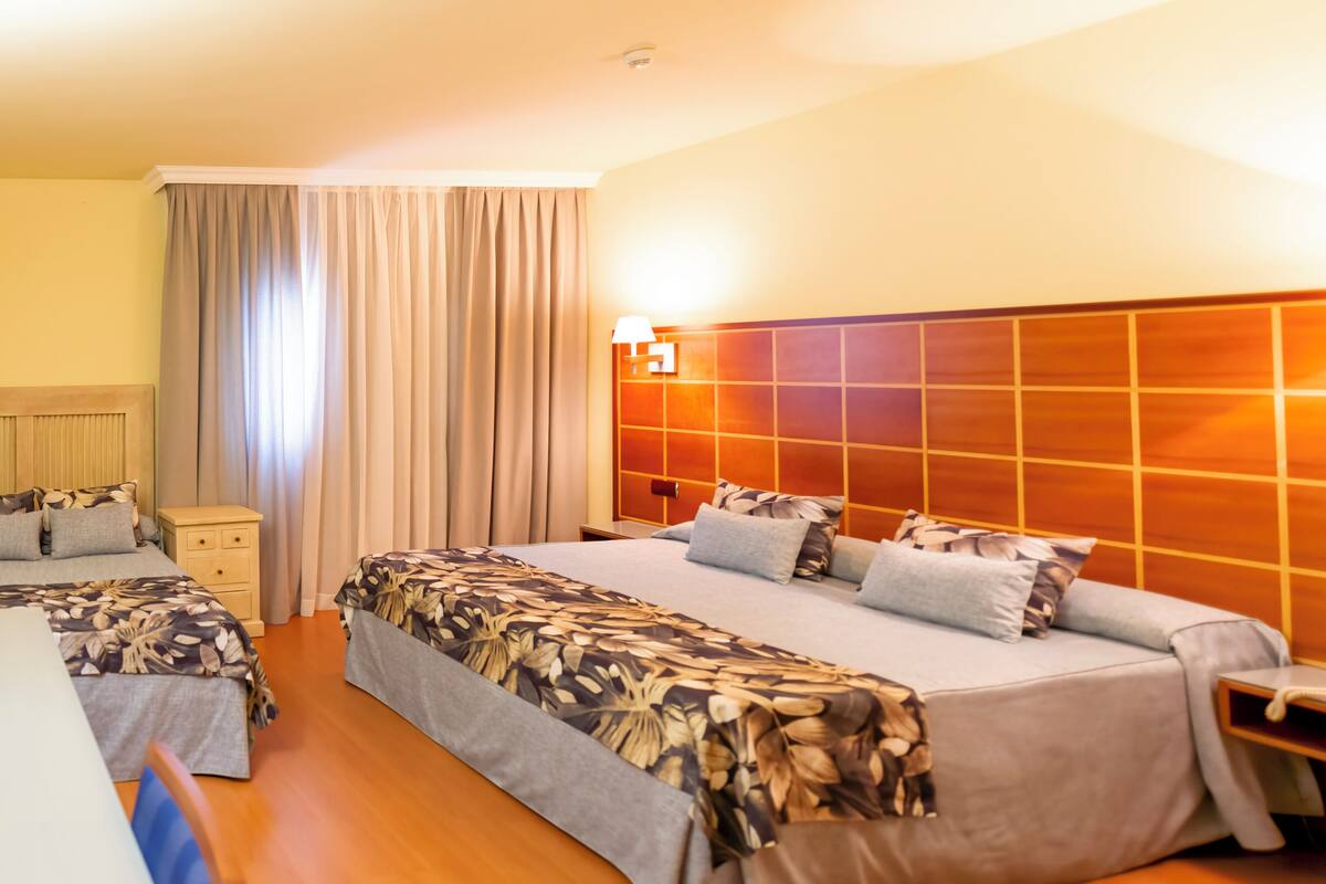 Habitación de hotel con dos camas, cabecero de madera, mesita de noche y lámpara.