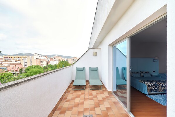 A balcony with two lounge chairs, a bed with a floral bedspread, and a city view. - Ramblas Vendrell (El Vendrell)