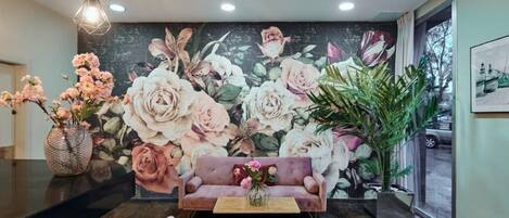 A reception area with a large floral mural, a sofa, a coffee table, and a vase of flowers.