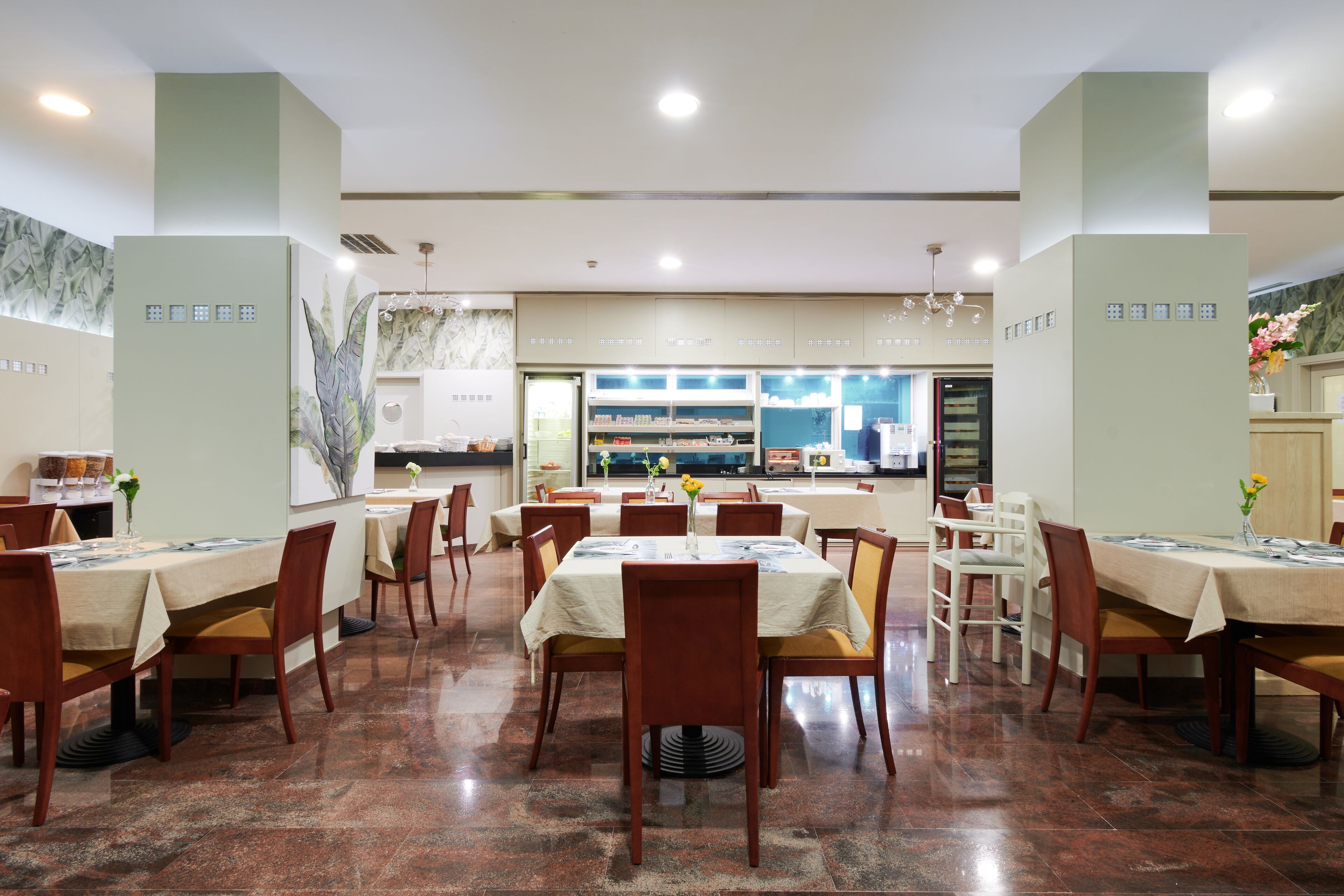 Un'ampia sala da pranzo con numerosi tavoli e sedie, una cucina sullo sfondo e un design d'interni moderno.