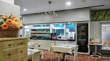 Een restaurant met een buffetopstelling, inclusief een toonbank met gerechten en een presentatie van flessen drank. Er staan eettafels met stoelen, en een decoratieve mand met bloemen op een kast.