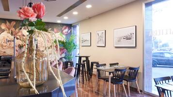 A restaurant interior with a counter, chairs, and tables. There are framed pictures on the wall and a vase with flowers on the counter.