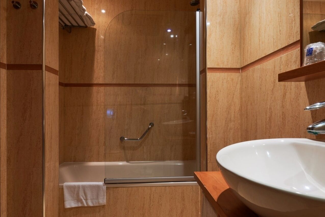 A modern bathroom with a glass-enclosed shower, a white sink, and wooden cabinetry.