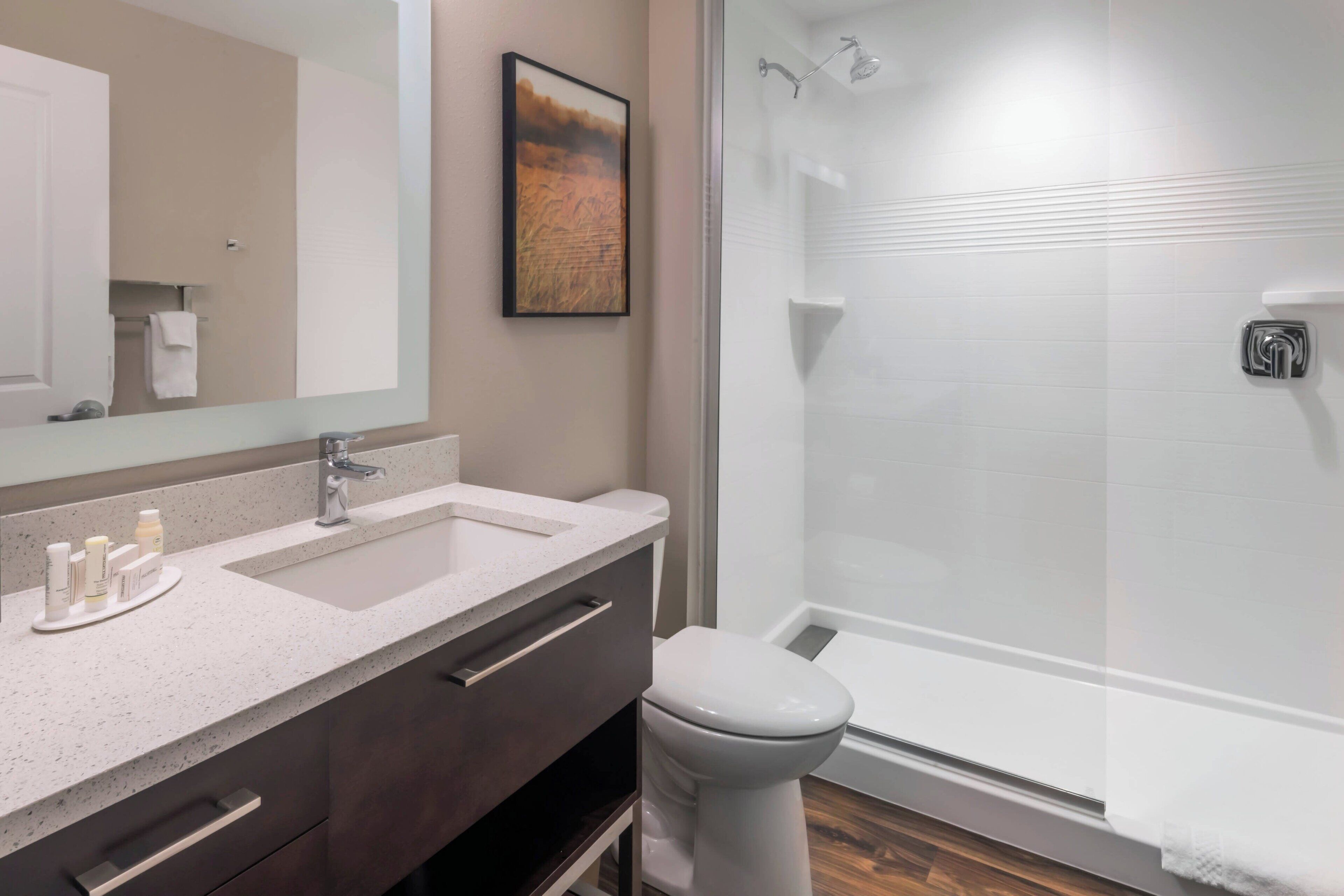 Un baño moderno con un espejo grande, un lavamanos, un inodoro y una ducha con mampara de vidrio.