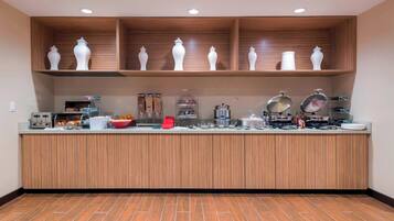 A kitchen area with wooden cabinets, a countertop with various appliances and food items, and a tiled floor.