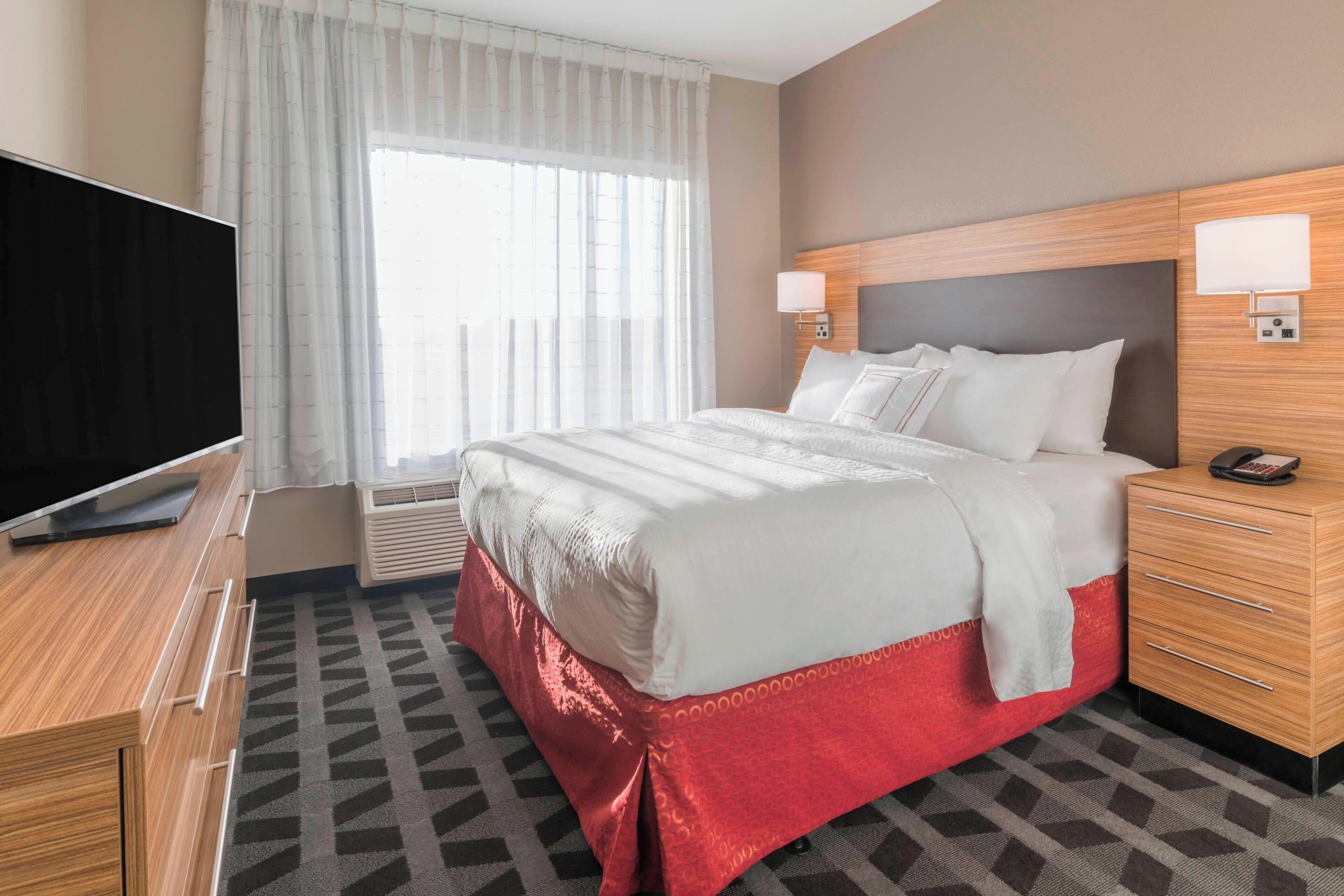 A hotel room with a large bed, a TV, a desk, and a window with curtains.