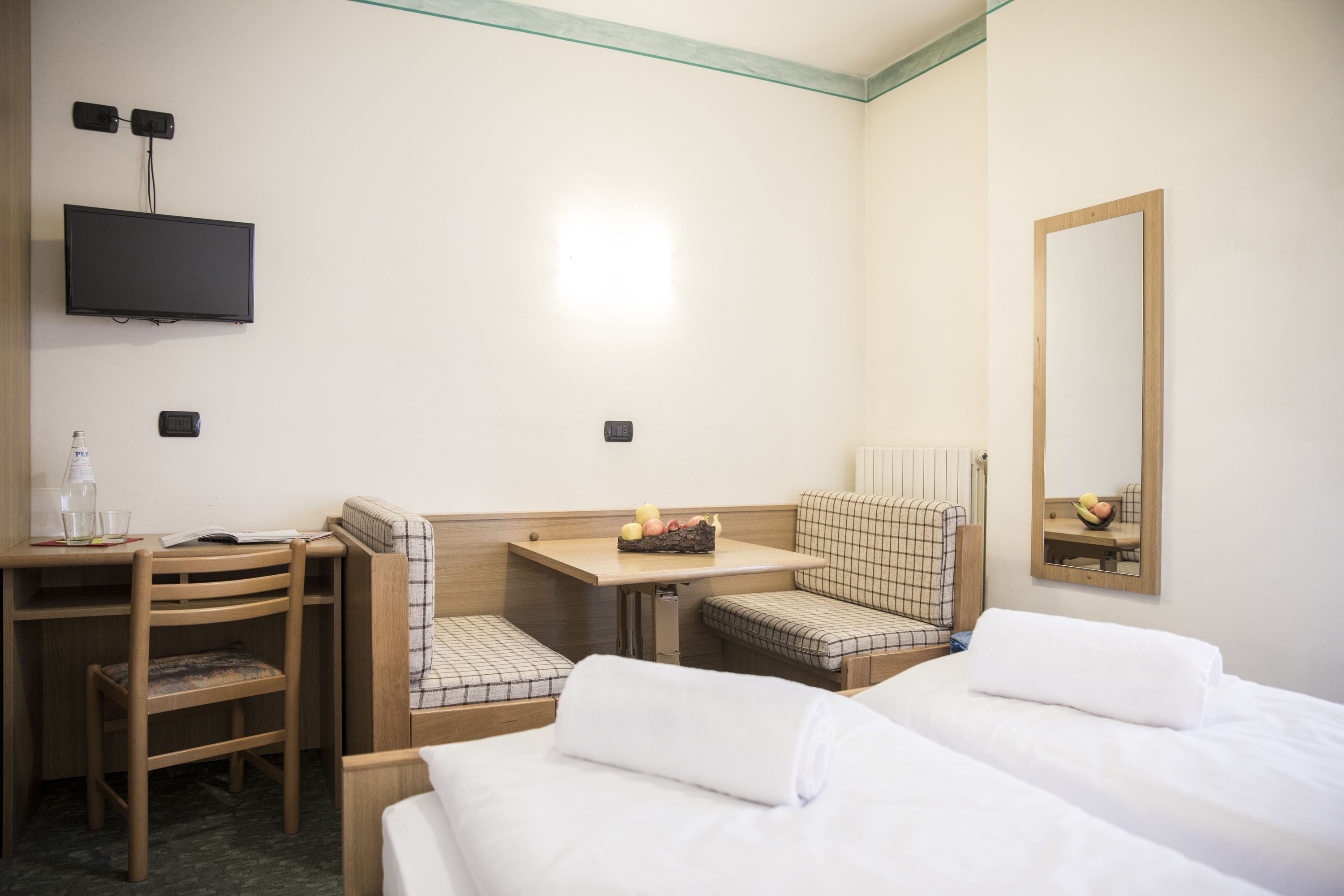 A hotel room with two beds, a desk, a chair, a television, and a mirror.