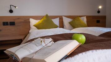 Un lit bien fait, avec une couverture marron, deux oreillers, une pomme verte et un livre ouvert sur lequel reposent des lunettes.