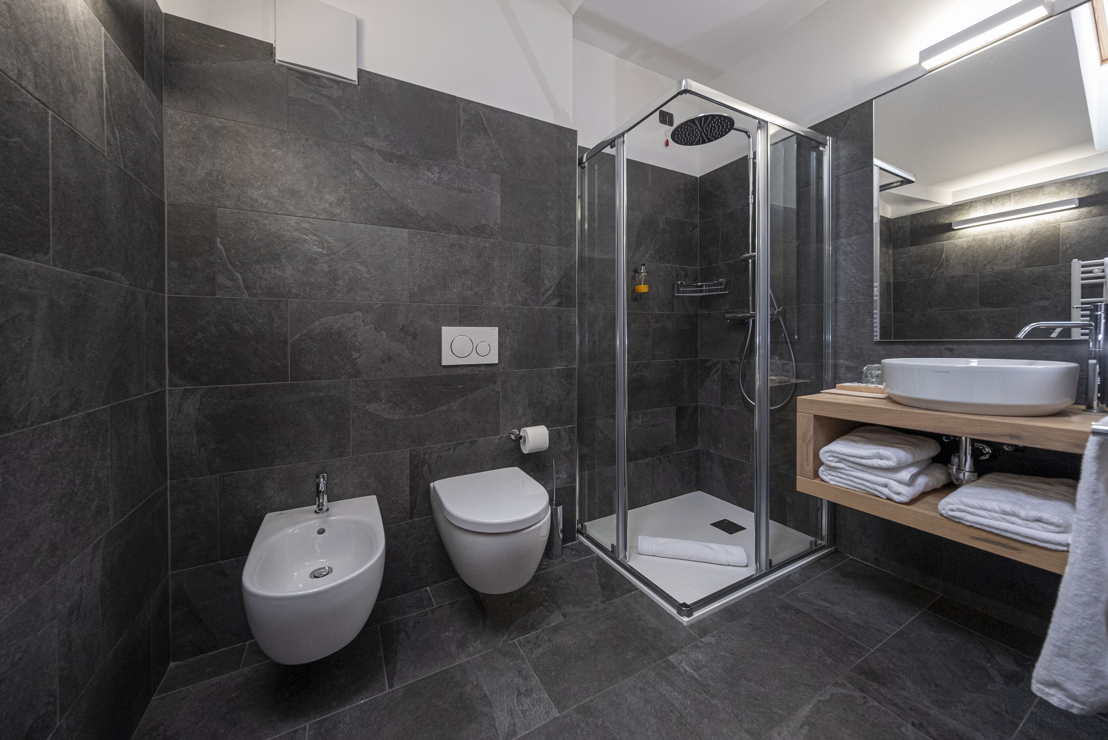 Een moderne badkamer met een glazen douchecabine, een bidet, toilet en een wastafelmeubel met wastafel en handdoekhouder.