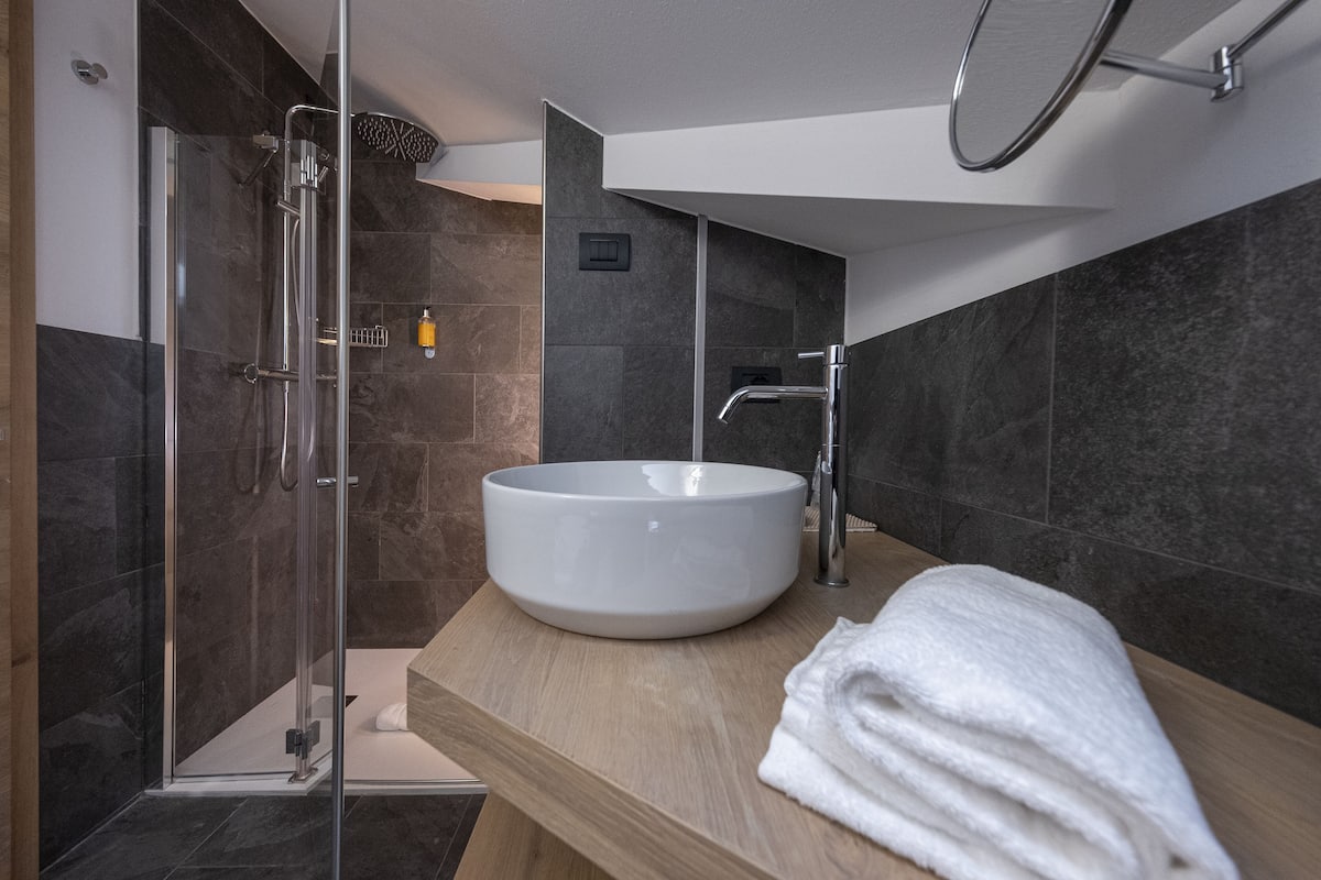 Un baño moderno con ducha envuelta en vidrio, un lavamanos grande de color blanco y una encimera de madera.