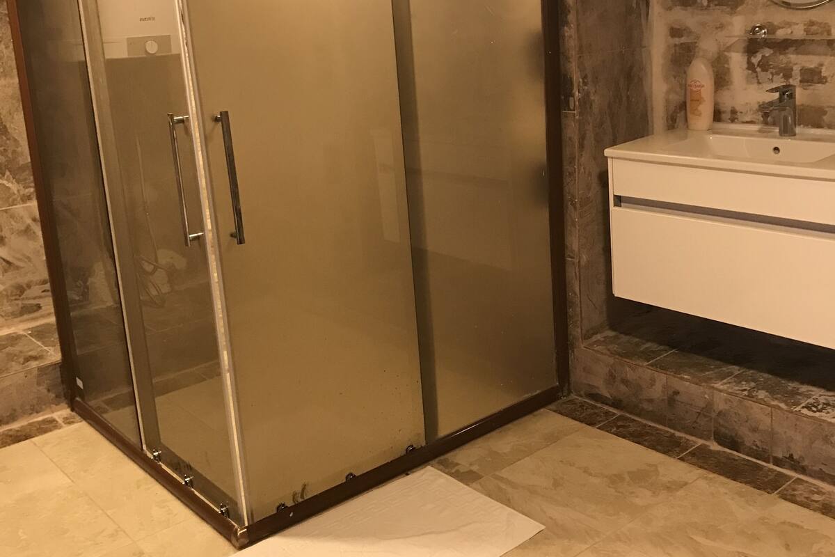 A bathroom with a glass-enclosed shower, a sink with a mirror, and a tiled floor.