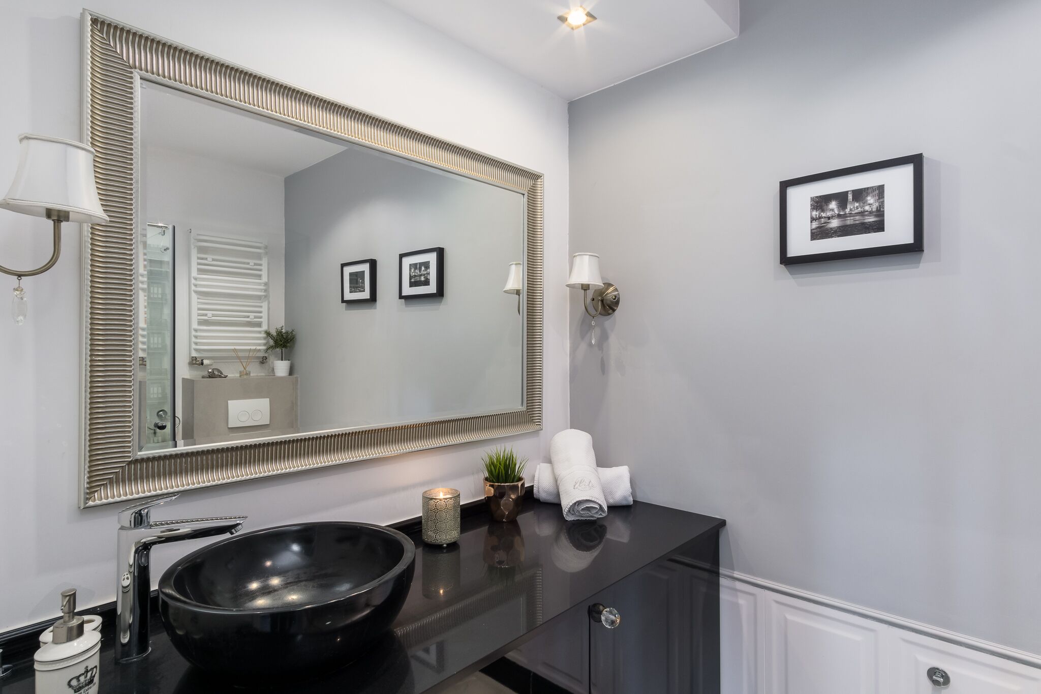 A modern bathroom with a large mirror, black sink, and a small potted plant.