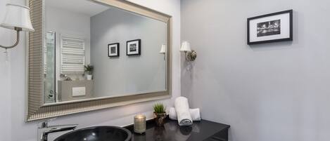 A modern bathroom with a large mirror, black sink, and a small potted plant.