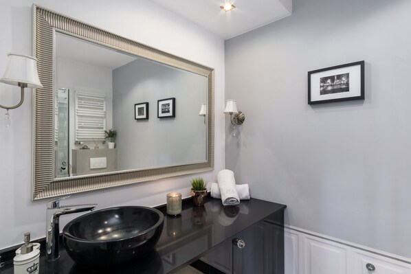Un baño moderno con un espejo grande, lavamanos negro y una pequeña planta en maceta.