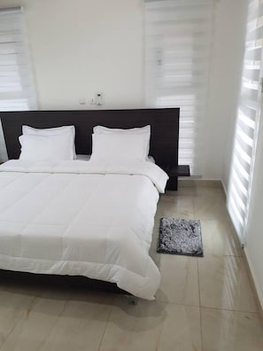 A neatly made bed with white bedding in a room with a dark headboard and light-colored walls. - Blue Sky Abissa 1 (Assinie)