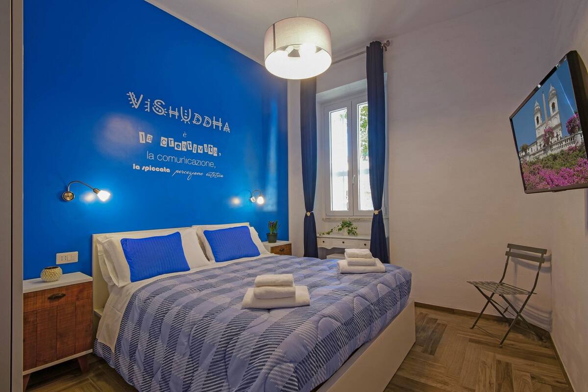 A bedroom with a blue accent wall, a bed with blue and white bedding, a nightstand, a lamp, and a window with curtains.