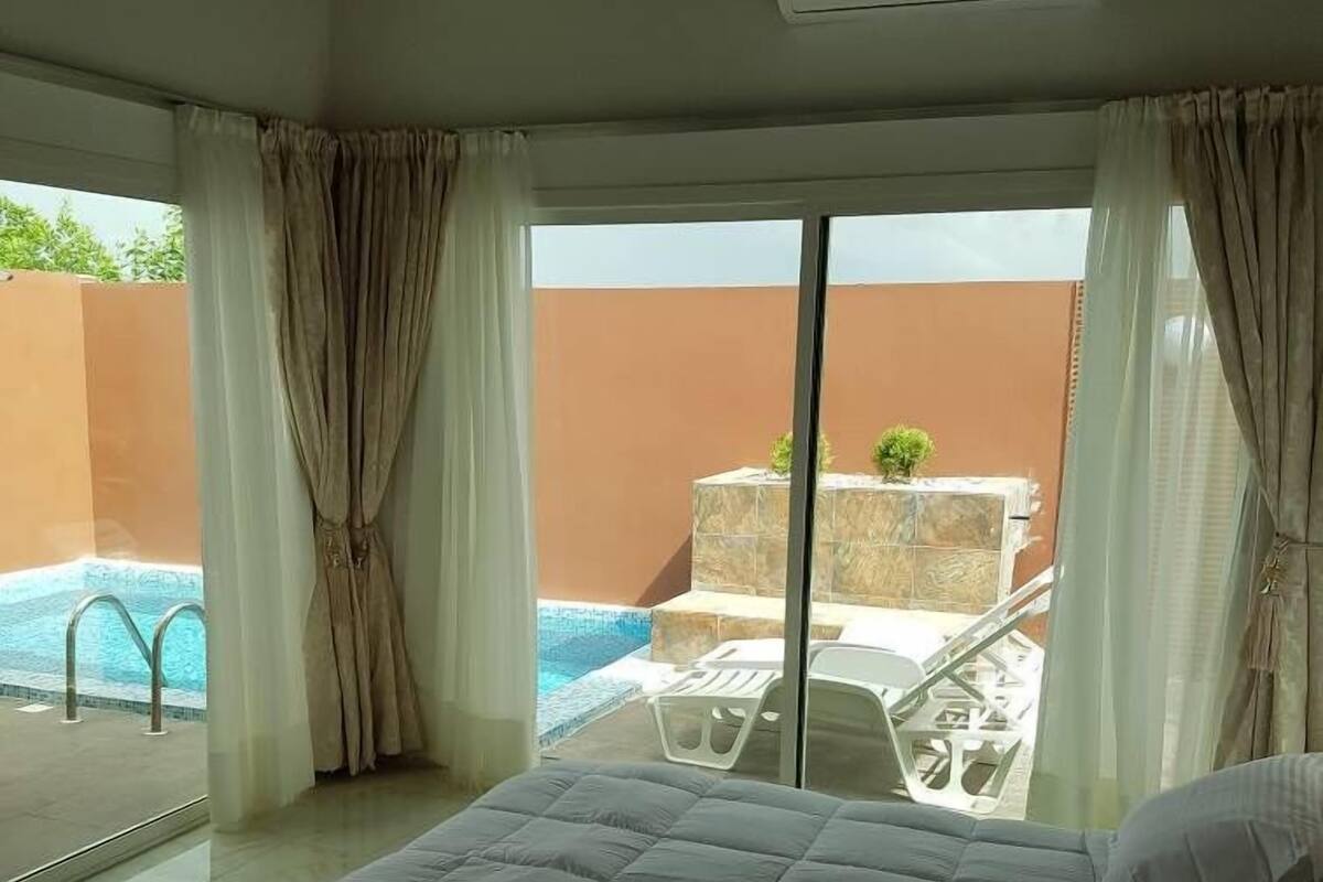 A bedroom with a bed, a view of a swimming pool, and a balcony with a chair.