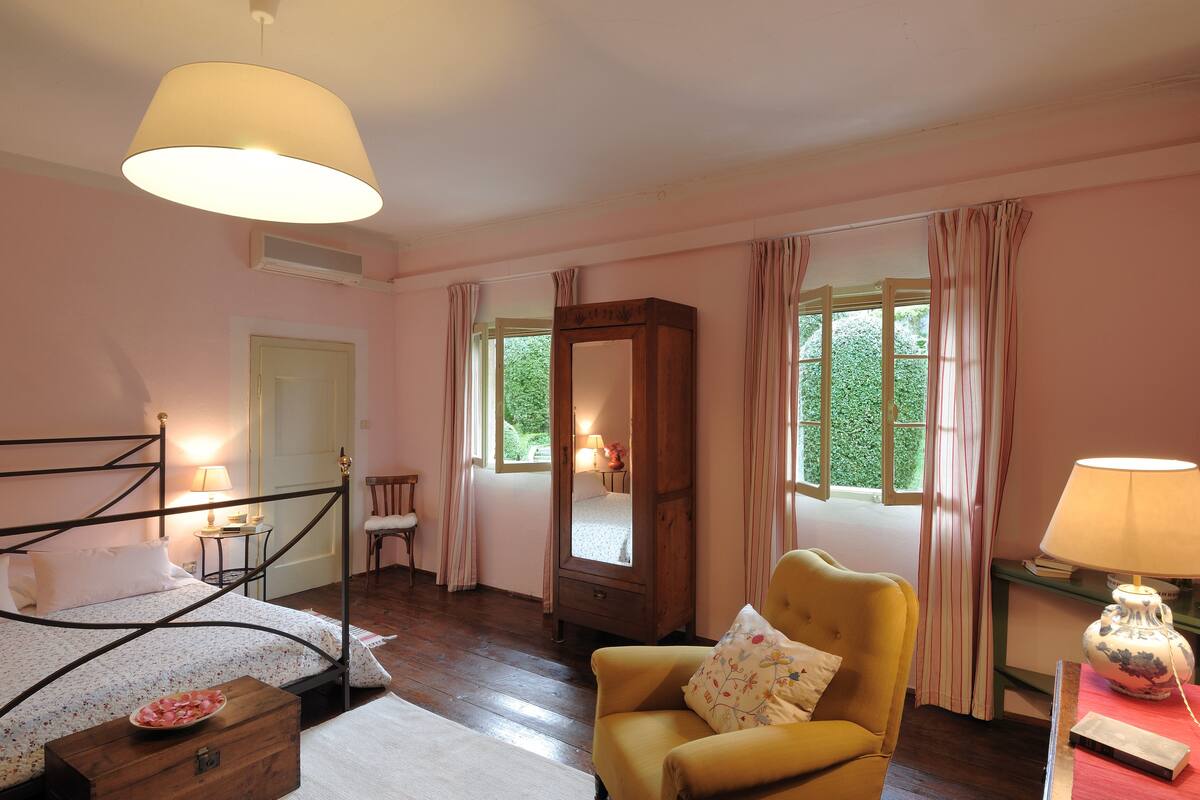 A bedroom with a bed, a chair, a mirror, and a window with curtains.