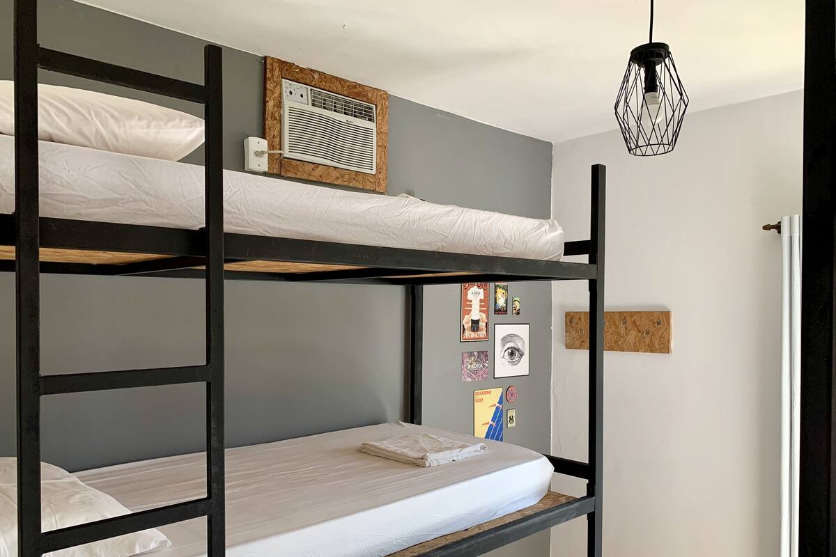 A bunk bed room with a ceiling fan, a wall-mounted air conditioner, and a door with a handle.