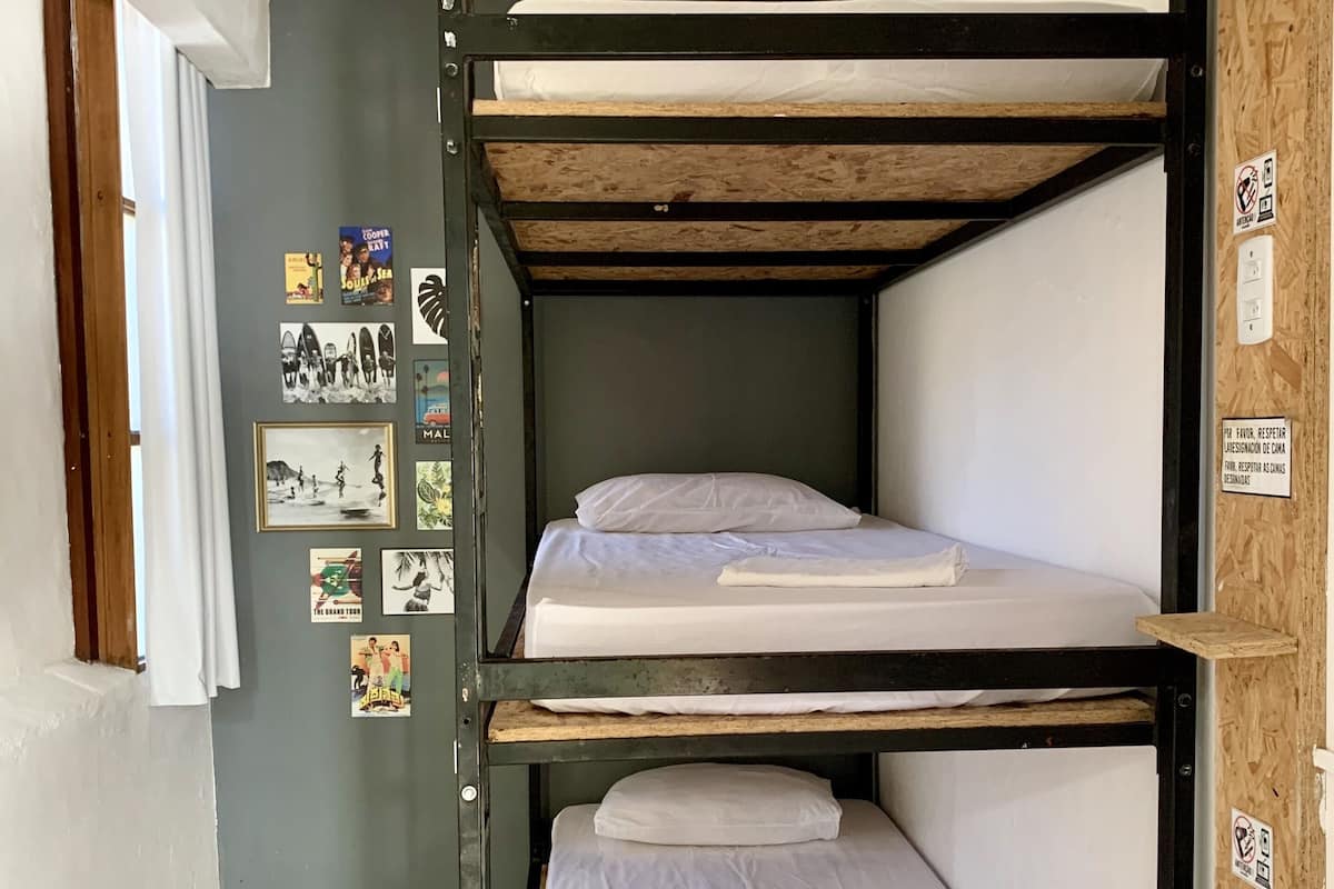 A bunk bed room with a wooden bunk bed structure, a tiled floor, and a wall with various posters.